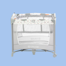 Load image into Gallery viewer, A compact playard known as Mini Cribette with white mesh on all four sides and a patterned sheet with the text 'Mini Cribette' on it. The product has wheels for portability and is set against a blue background.